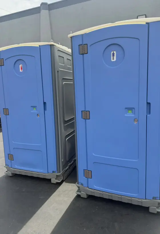 Two blue standard porta potties with men and women door signs, ready for delivery